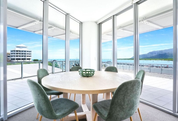 Un salón de conferencias con una mesa redonda y sillas, amplias ventanas que ofrecen vistas a un edificio y una masa de agua.