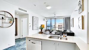A modern kitchen with a dishwasher, a dining area with a table and chairs, and a view of the outside. - 901 Harbour Lights- Luxury 2BR Waterfront Apartment | Stunning Marina Views | Pool + Sauna (Cairns City)