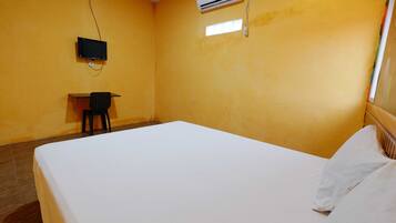 A room with a bed, a desk, a chair, an air conditioning unit, and a television.