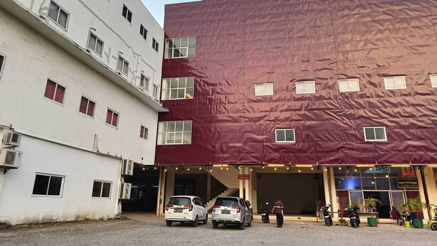 Ein mehrgeschossiges Gebäude mit roter Fassade und ein angrenzendes weißes Gebäude. Autos sind vor dem Haus geparkt, und eine Person geht in der Nähe des Eingangs entlang.