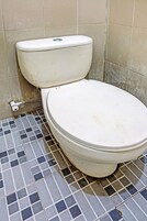 Sanitário com assento e tampa brancos, posicionado contra uma parede com azulejos bege.