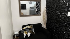 A modern living room with a black sofa, a geometric-patterned wall, a mirror, and a small side table. - Lovely 1BR Condo SM Southmall 100mbps Netflix Disney+ (Las Piñas)