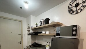 A compact kitchen with a refrigerator, microwave, and a clock on the wall. - Lovely 1BR Condo SM Southmall 100mbps Netflix Disney+ (Las Piñas)