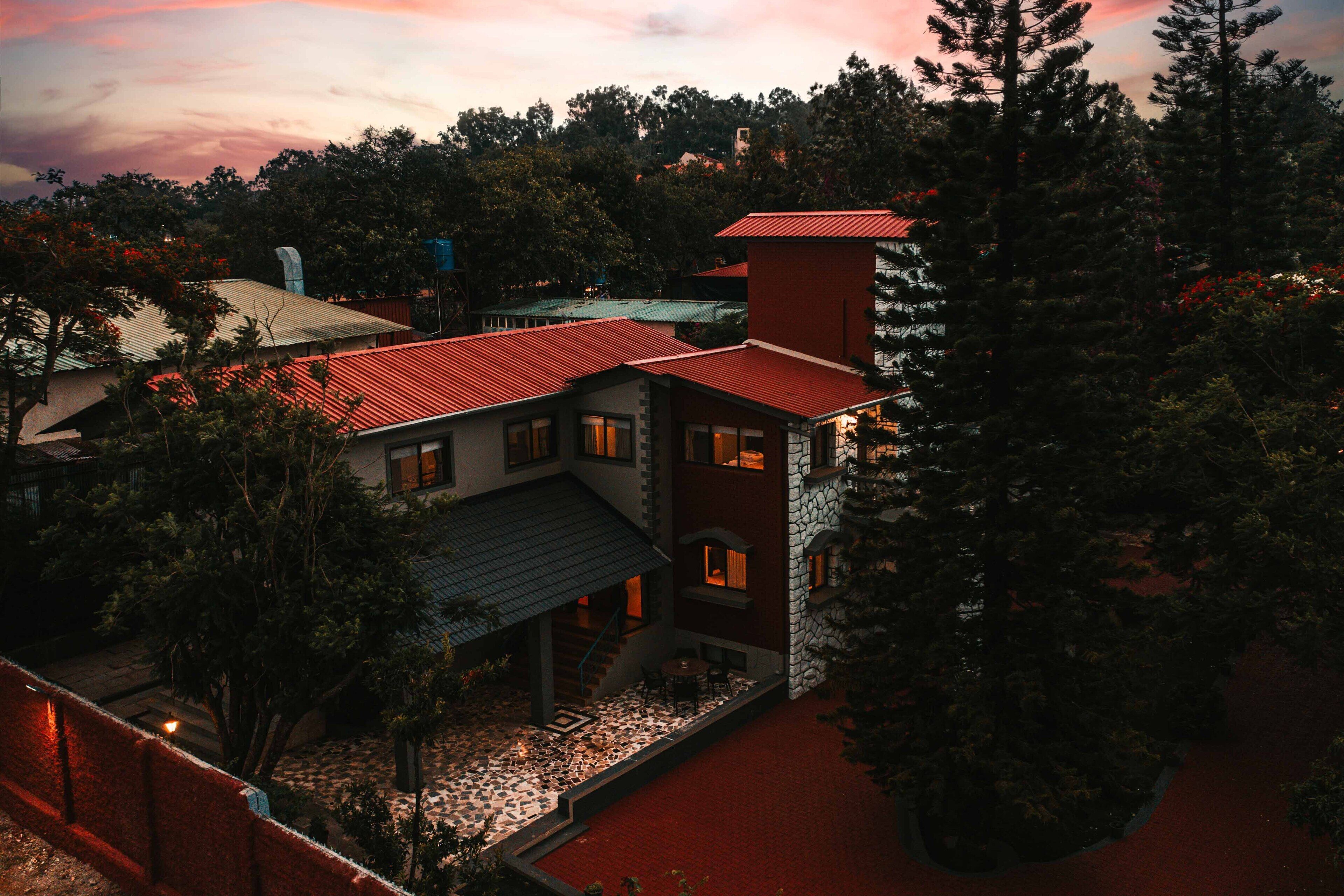 A multi-story building with a red roof, surrounded by trees and a paved courtyard.