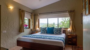 Un dormitorio con una cama grande, dos mesitas de noche, una ventana con cortinas y vistas a zonas verdes.