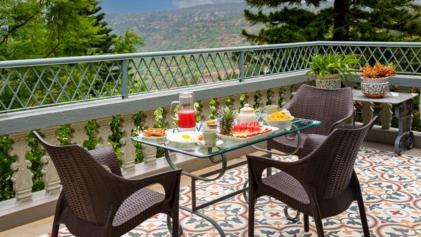 Un balcón con sillas de mimbre, una mesa de vidrio y vistas a un paisaje montañoso.