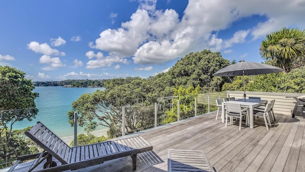 A wooden deck with a table and chairs, overlooking a body of water and a distant shoreline. - Absolute Beachfront - Oneroa Bay (Auckland)