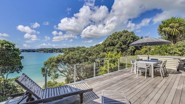 A wooden deck with a table and chairs, overlooking a body of water and a distant shoreline. - Absolute Beachfront - Oneroa Bay (Auckland)