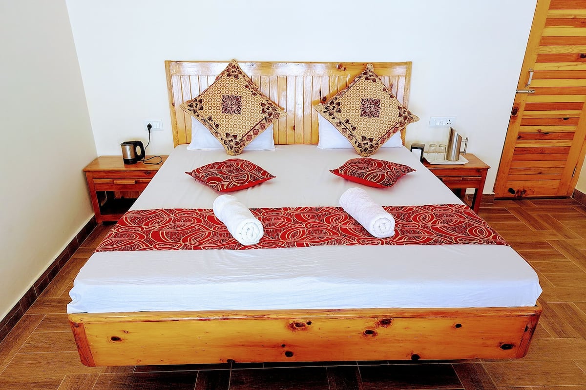 Una cama con estructura de madera, dos almohadas, una toalla enrollada y una mesita de noche con una lámpara.