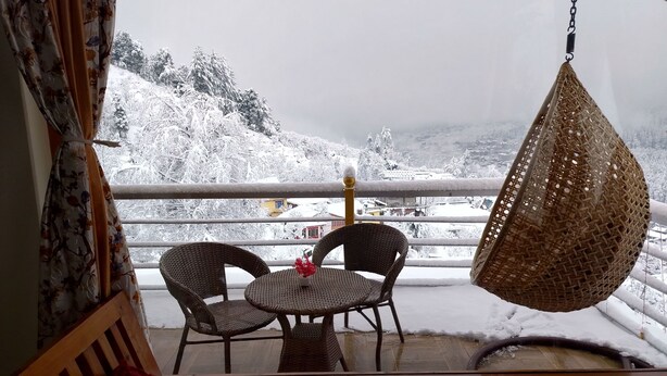 Een balkon met rieten stoelen en een hangstoel, met uitzicht op een besneeerd landschap.