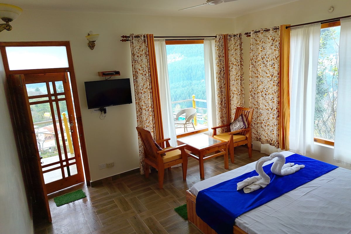 Habitación de hotel con cama, escritorio, dos sillas, televisor y balcón con vistas.