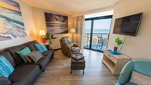 A modern living room with a sofa, armchair, and a small table. There is a TV mounted on the wall and a balcony with a view of the ocean. - 3BR in Sand Dunes Resort Ocean View - Great Views (Myrtle Beach)