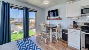 Eine moderne Küche mit Mikrowelle, Backofen und einem Fernseher, der über der Arbeitsplatte angebracht ist. Ein Essbereich mit Tisch und Stühlen sowie ein großes Fenster mit Vorhängen sind ebenfalls vorhanden.