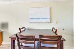 A dining table with four chairs, a painting on the wall, and a light switch.
