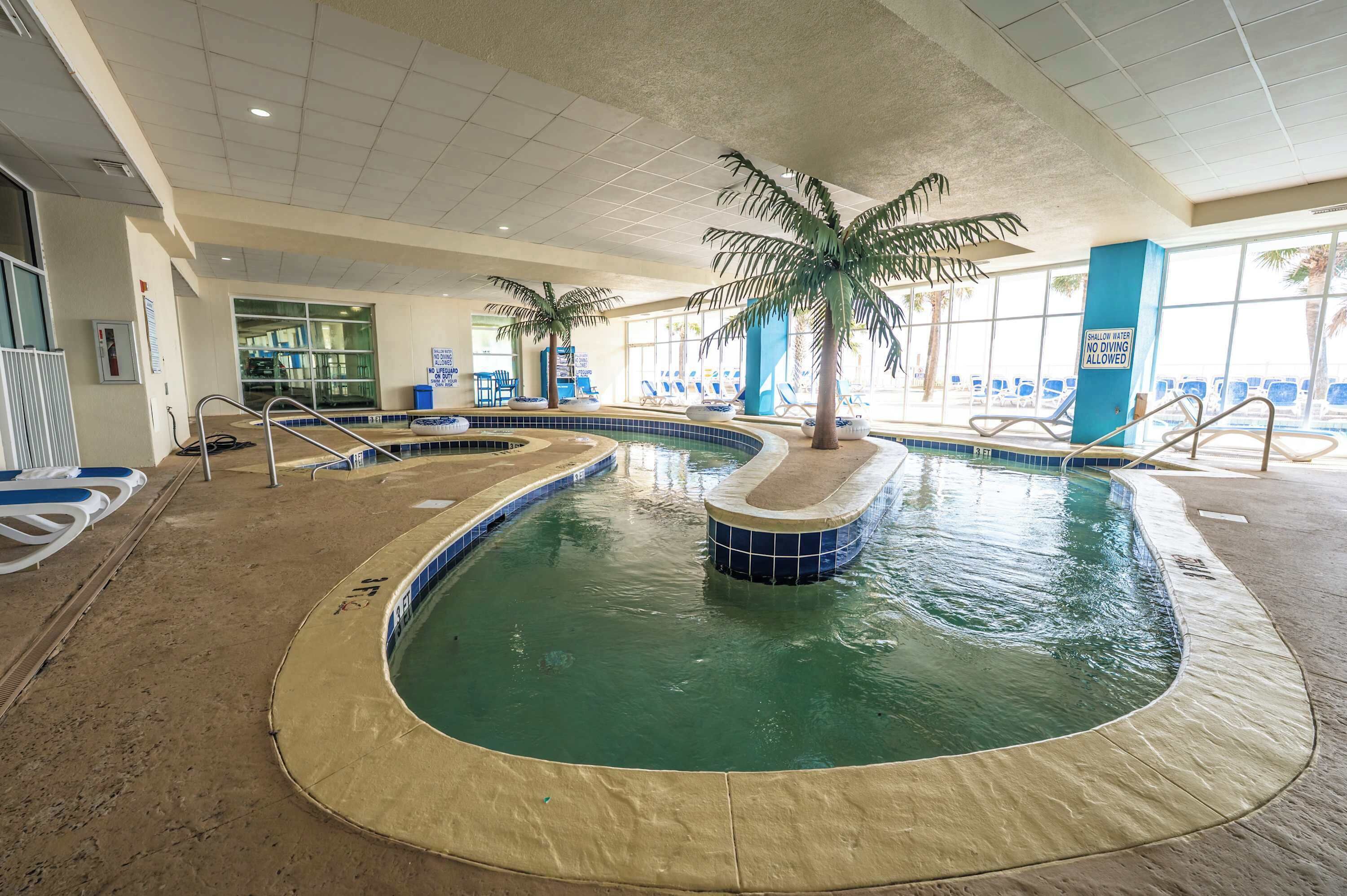An indoor swimming pool with multiple lanes, palm trees, and lounge chairs.