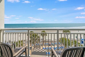 Un balcon avec vue sur la plage, des chaises longues et des palmiers.