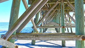 A wooden pier structure with a clear view of the ocean and beach.