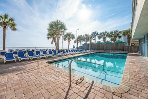 A pool area with blue lounge chairs and palm trees.