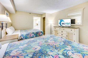 A hotel room with two beds, a TV, a dresser, and a lamp.