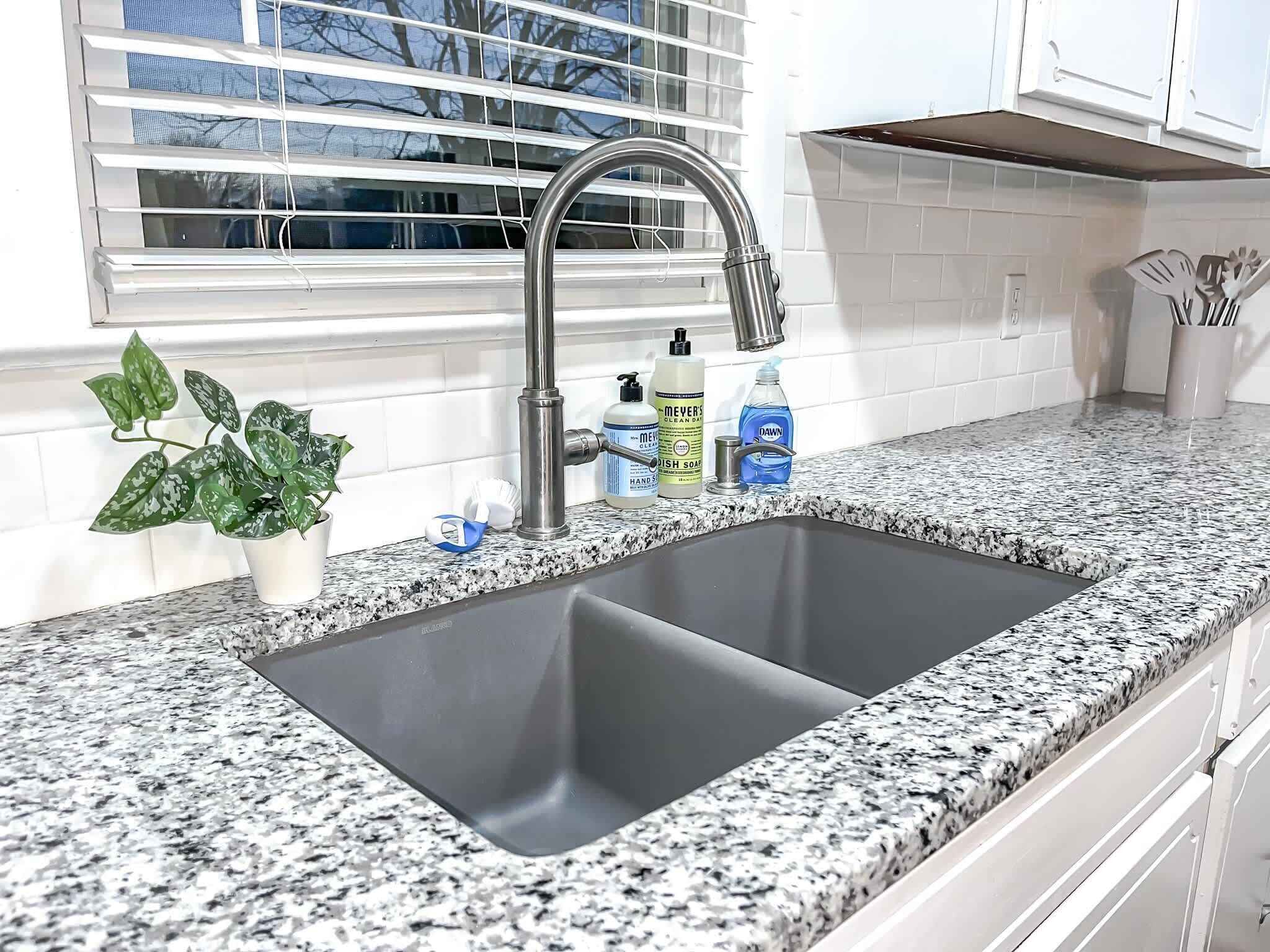 Una cocina con un lavamanos doble, encimera de granito y una ventana con persianas.