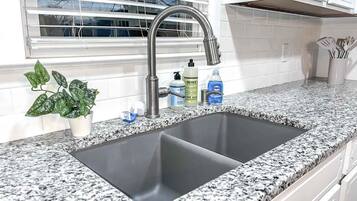 Una cocina con un lavamanos doble, encimera de granito y una ventana con persianas.