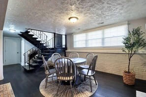 Un coin repas avec une table ronde et des chaises, un escalier et une plante.