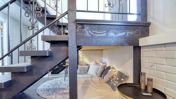 A loft bedroom with a bed, a small table, and a staircase.