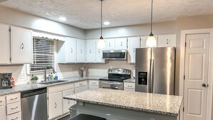 A modern kitchen with white cabinets, granite countertops, stainless steel appliances, and pendant lighting.