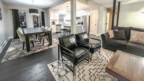 A modern living room with a dark wood floor, a patterned rug, a leather sofa, and a dining area with a dark wood table and chairs.