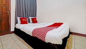 A neatly made bed with a red and white patterned blanket, two red pillows, and grey curtains. - Hotel O Fj Guest House (Cileunyi)