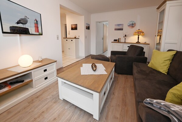 Una sala de estar con una mesa de centro de madera, un sofá marrón con cojines amarillos, un mueble de televisión blanco y una lámpara.