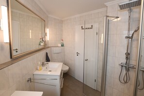 A modern bathroom with a large mirror, a sink, a toilet, and a glass-enclosed shower area.