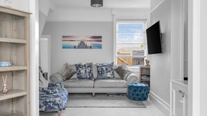 A modern living room with a grey sofa, blue patterned ottoman, and a flat-screen TV mounted on the wall. - Super Comfortable & High Quality (Cleethorpes)