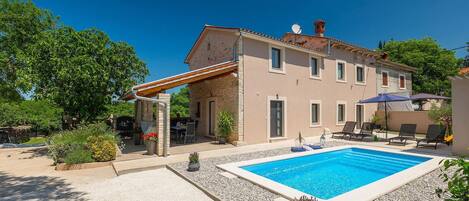 A two-story house with a swimming pool, outdoor seating, and a pergola.