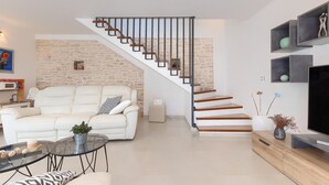 A modern living room with a white sofa, a glass coffee table, and a staircase with wooden steps and black railings. - Awesome home in Marcana (Marcana)