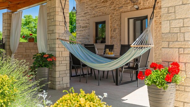 A hammock chair under a wooden pergola, a stone wall, and a table with chairs. - Awesome home in Marcana (Marcana)
