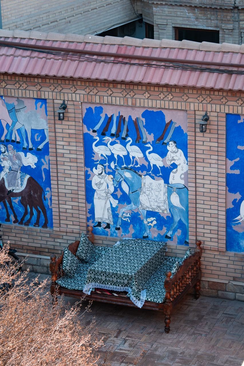 A bench with a patterned cover in front of a wall with murals.