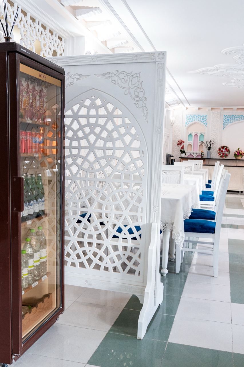A hotel lobby with a decorative partition, a wine refrigerator, and a seating area with blue cushions.