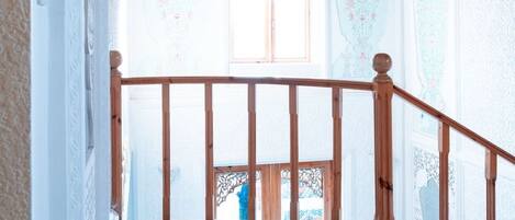 Un escalier recouvert d’une moquette à motifs mène à une pièce dotée d’un plafond en bois et d’une fenêtre ornée d’un motif décoratif.