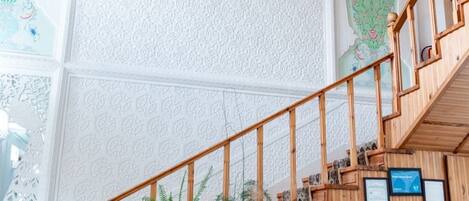 A wooden staircase with a railing, a hanging plant, and a wall with decorative panels.