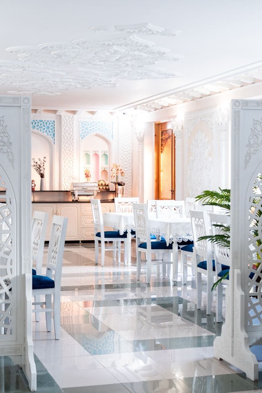 A dining area with white chairs and tables, a tiled floor, and ornate ceiling designs.