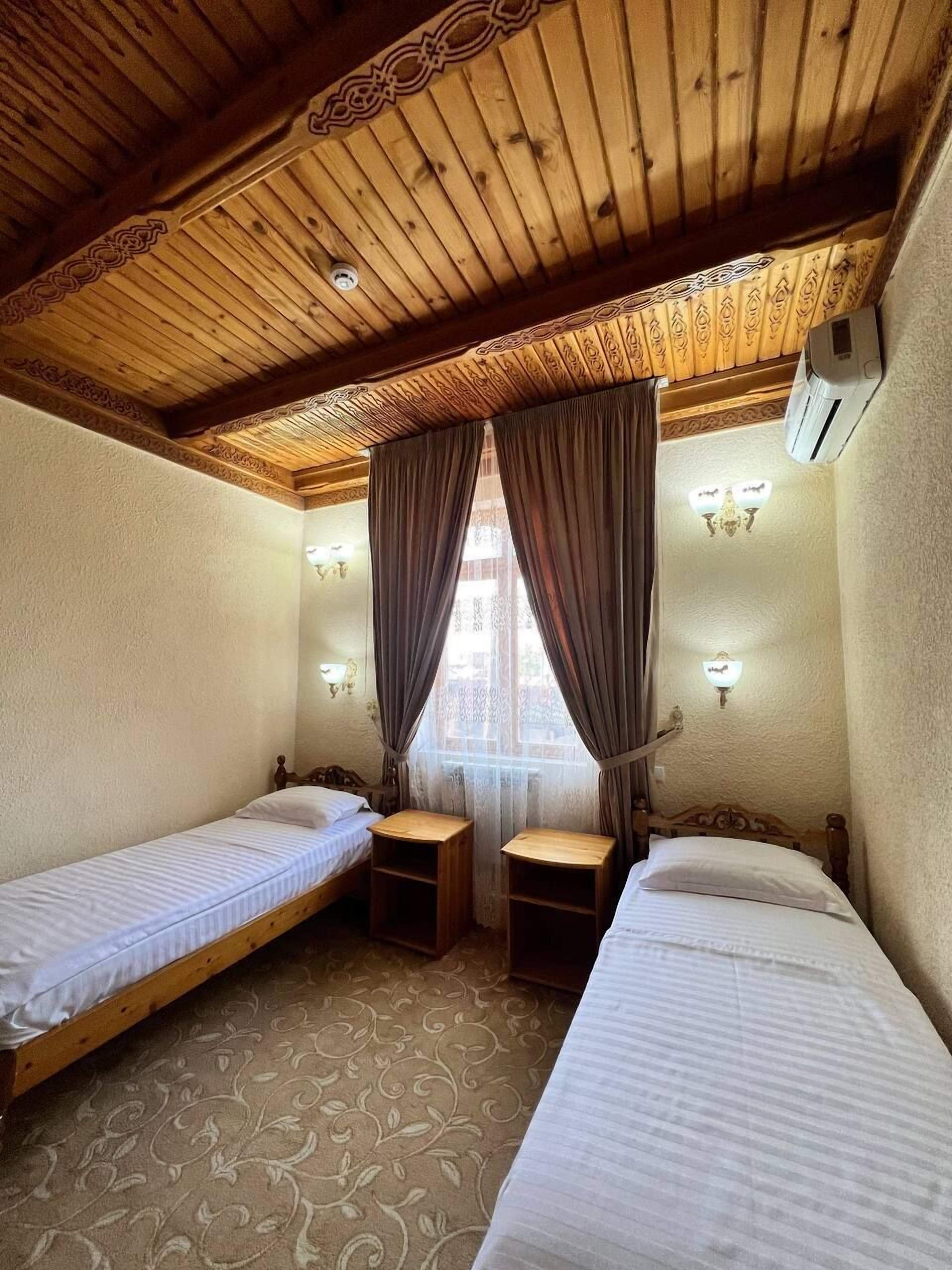Une chambre avec deux lits simples, une petite table et une fenêtre avec des rideaux.