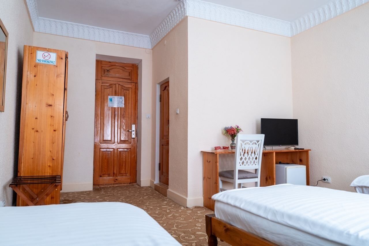 Une chambre d’hôtel avec deux lits, une armoire en bois, un bureau avec une chaise, une télévision et une porte sur laquelle est apposé un panneau « Interdiction de fumer ».