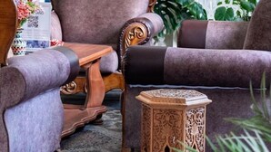 Una habitación con una gran silla ornamentada, un sillón más pequeño y una mesita de noche con intrincados grabados.