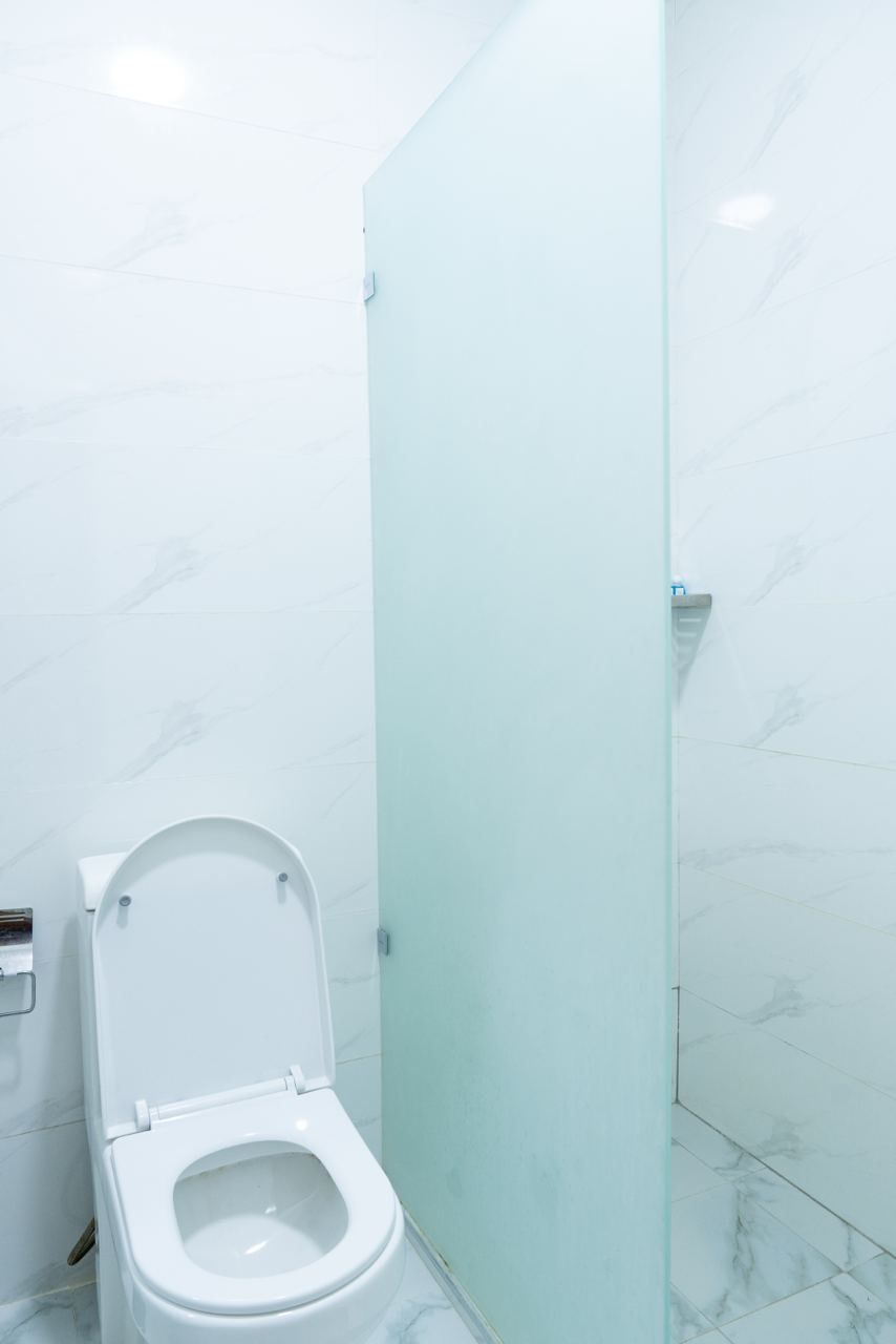 A bathroom with a toilet, a glass shower enclosure, and marble-patterned walls.