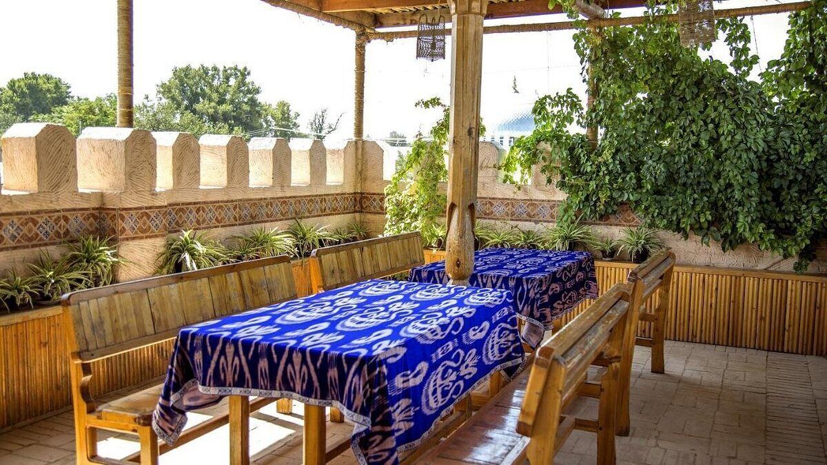 An outdoor patio with wooden benches and tables covered with blue tablecloths.