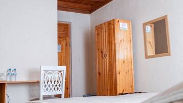 Una habitación con techo de madera, una cama con colcha marrón, una silla blanca, un armario de madera y un pequeño espejo en la pared.