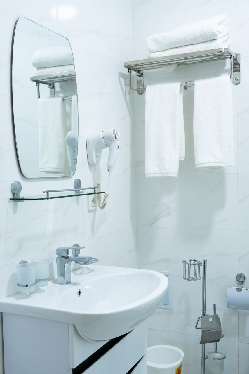 Un baño moderno con un lavabo blanco, un espejo, un perchero para toallas y un secador de pelo.