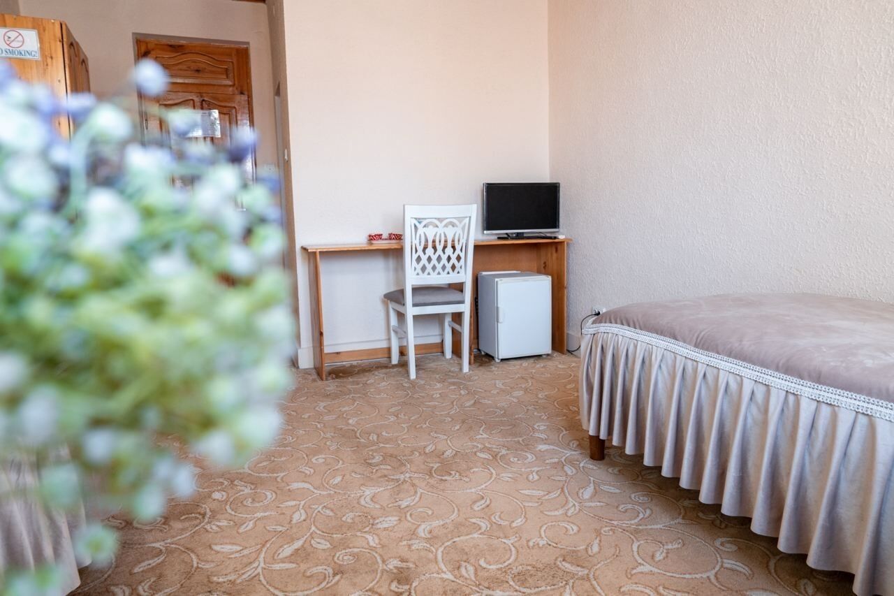A hotel room with a bed, a desk with a computer, a chair, and a television.