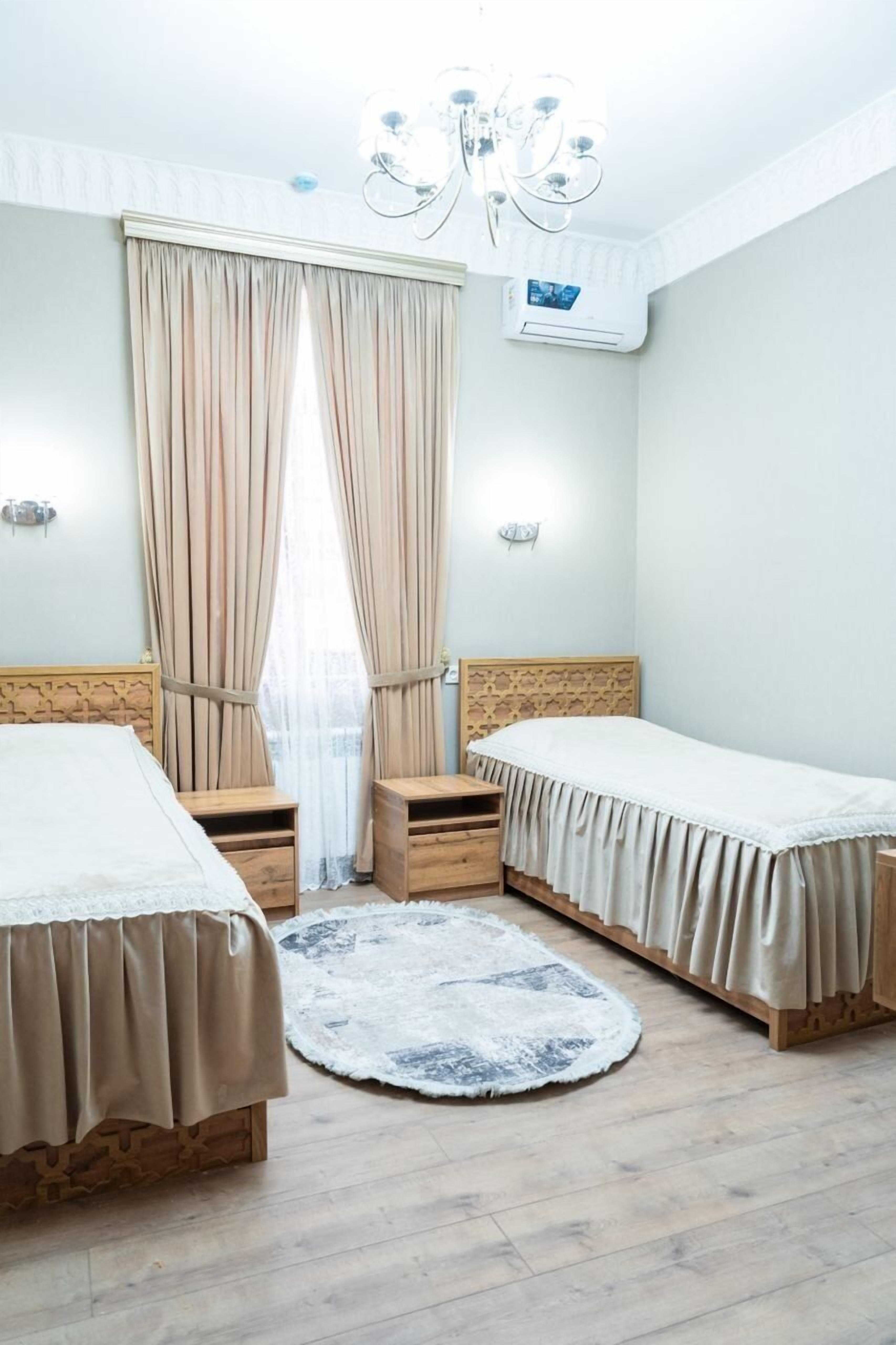 A bedroom with two beds, a chandelier, a round rug, and an air conditioning unit.